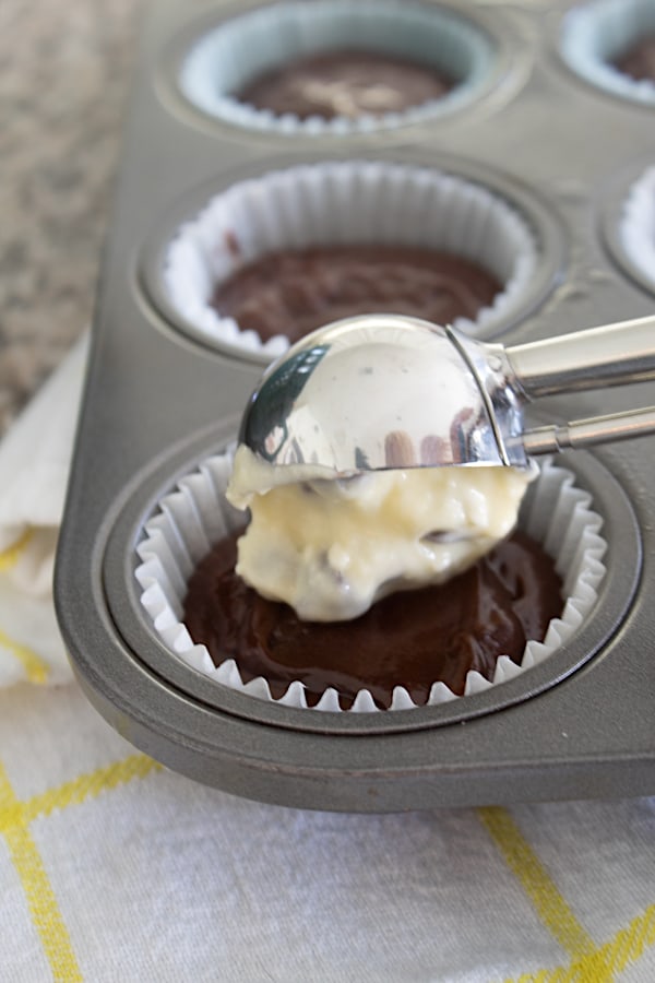 adding scoop of cream cheese filling to cupcake pan
