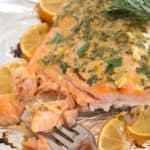 salmon on sheet pan with herbs and lemon slices cooked to perfection with fork taking a bite