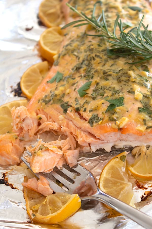 salmon on sheet pan with herbs and lemon slices cooked to perfection with fork taking a bite