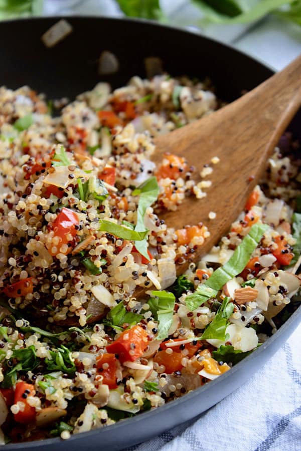 pan full of quinoa pilaf with a wooden spoon and scallion garnish
