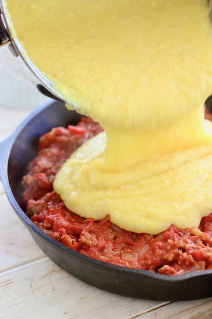 pouring creamy polenta over sausage ragu