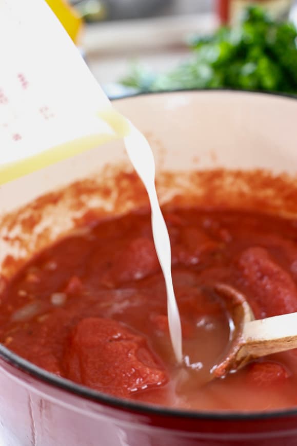 Chicken broth being poured into a large pot of tomato soup