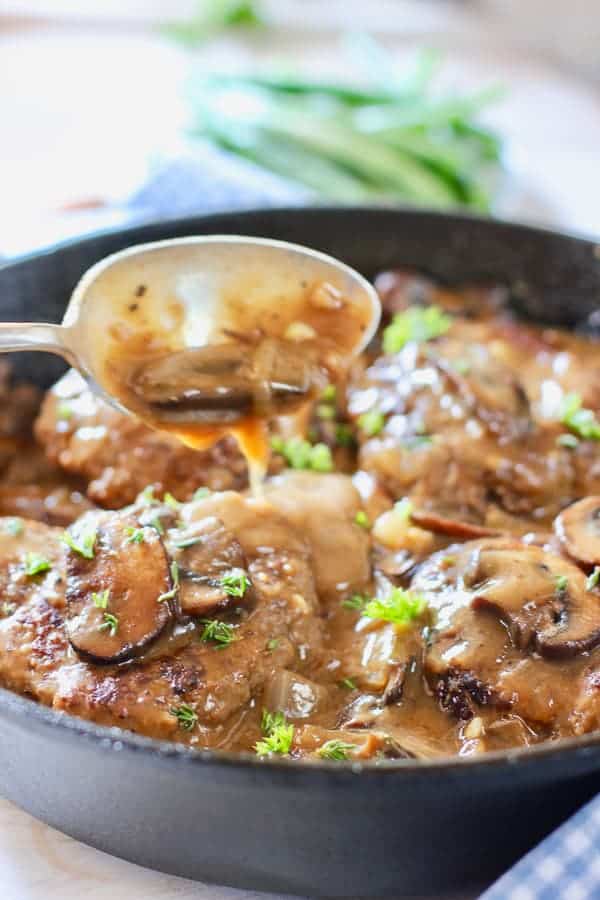 spooning gravy over Salisbury Steak