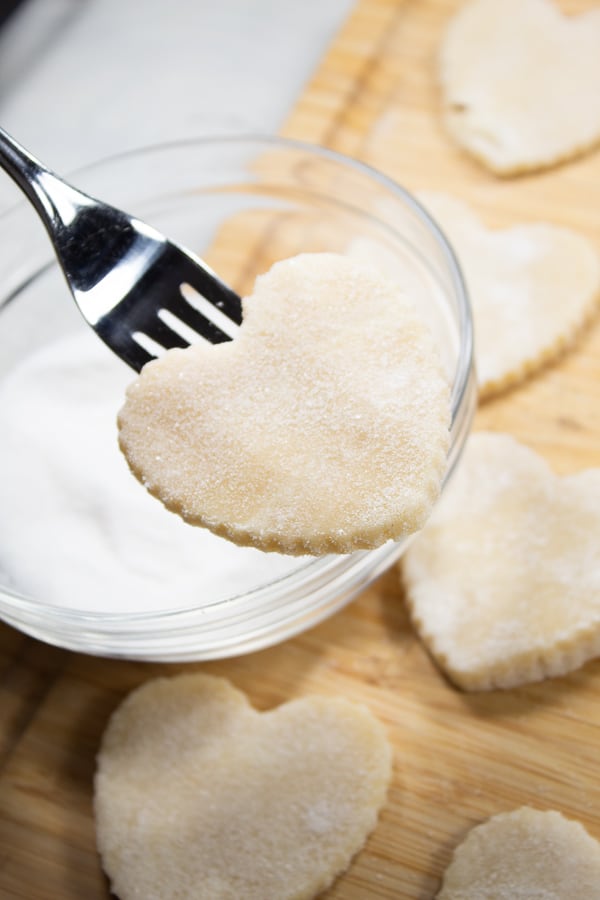 a clear bowl filled with sugar with a lifted fork with a raw cream wafer on it just dipped sugar