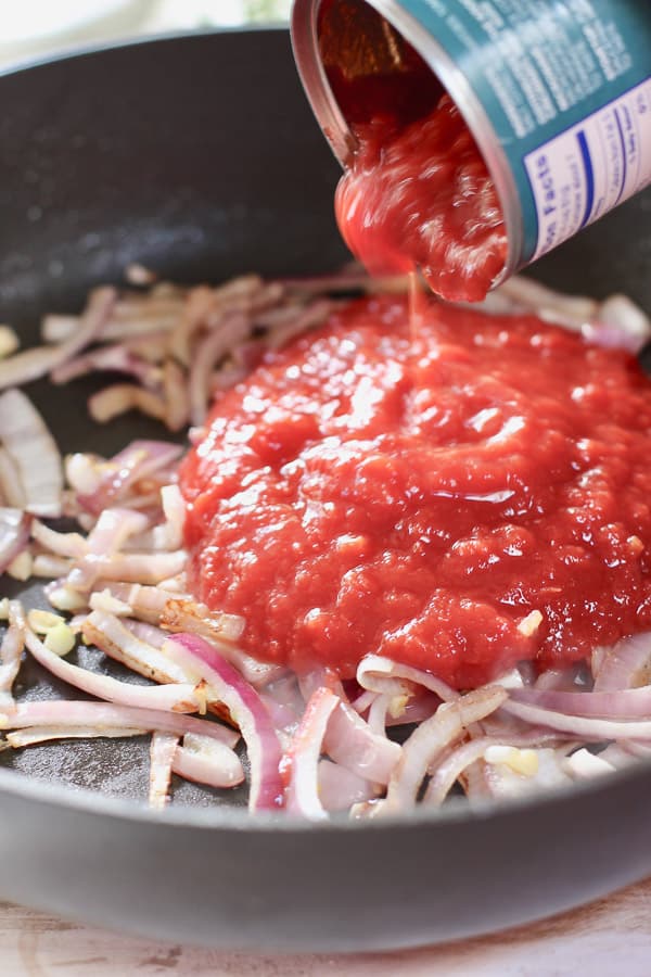 can of crushed tomatoes being added to sautéed onions and garlic