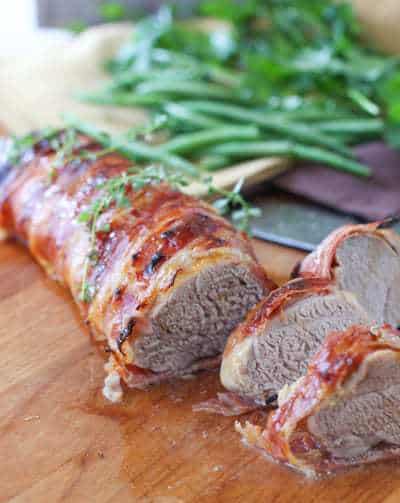 Prosciutto Wrapped Pork Tenderloin being sliced on a cutting board