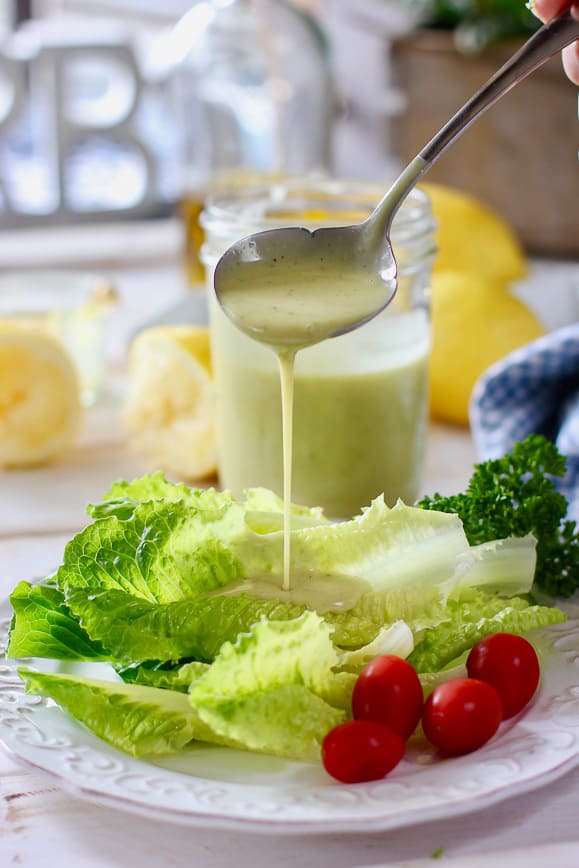 A ladle of vinaigrette being poured on fresh salad