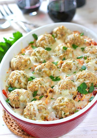 Meatballs and pasta in a casserole dish topped with melted parmesan, garnished with parsley.