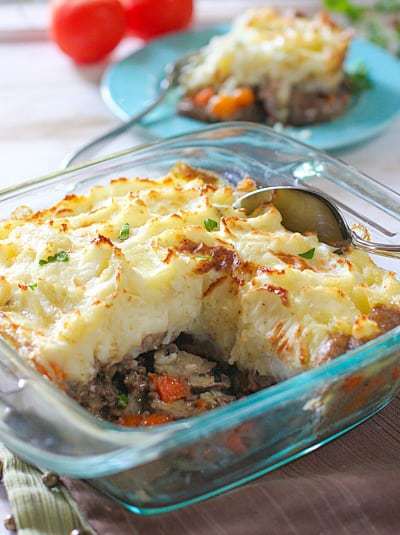 Shepherds Pie in a casserole dish with a spoon showing the inside of the casserole layers.