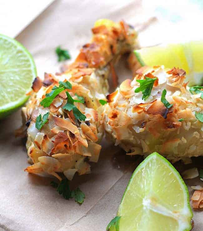 Toasted shredded coconut smothered chicken drumsticks garnished with cilantro and lime wedges