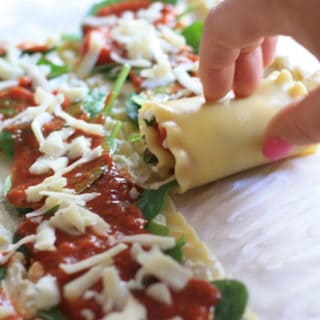 Lasagna roll ups on a parchment sheet filled with ricotta, spinach, marinara and grated parmesan cheese