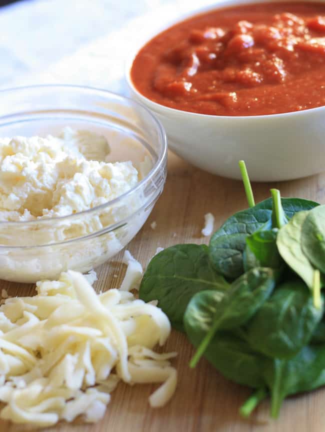 A plate of lasagna roll up filling ingredients; ricotta, shredded mozzarella, spinach and marinara sauce.