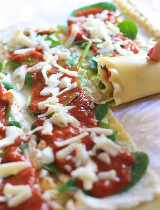 Rolling lasagna roll ups on a parchment sheet.