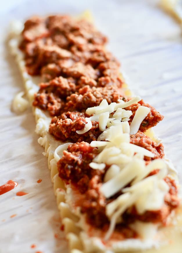 Lasagna roll up laid out with ricotta, meat filling, and parmesan cheese.