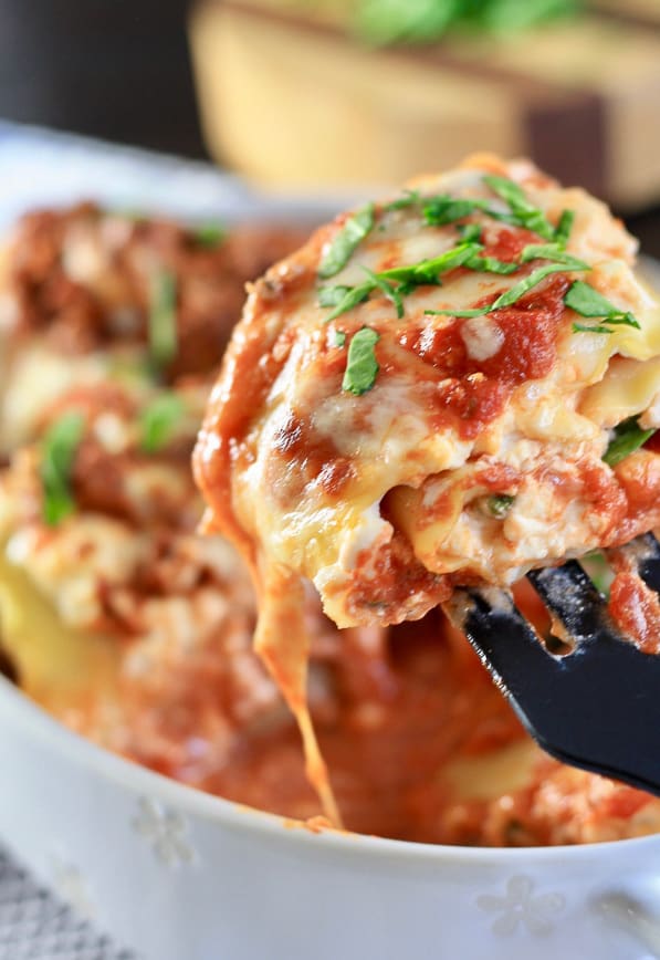 Lasagna roll up on a spatula with the full dish in the background
