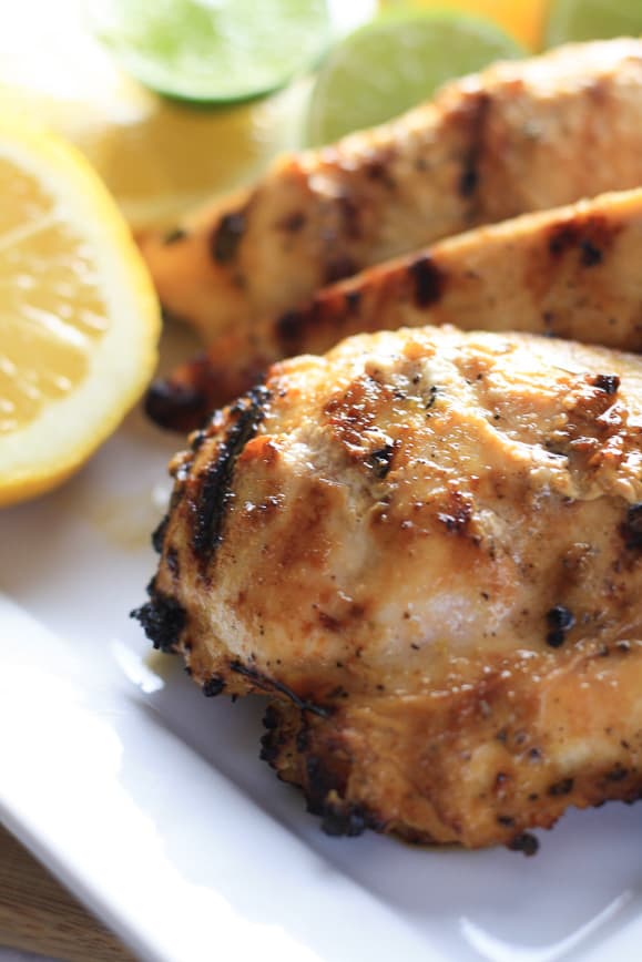 Lemon Grilled Chicken on a White Plate with Sliced Lemons and Limes in the Background