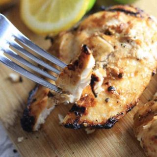 Lemon Grilled Chicken on a Cutiting Board being Sliced and Served with. Fork