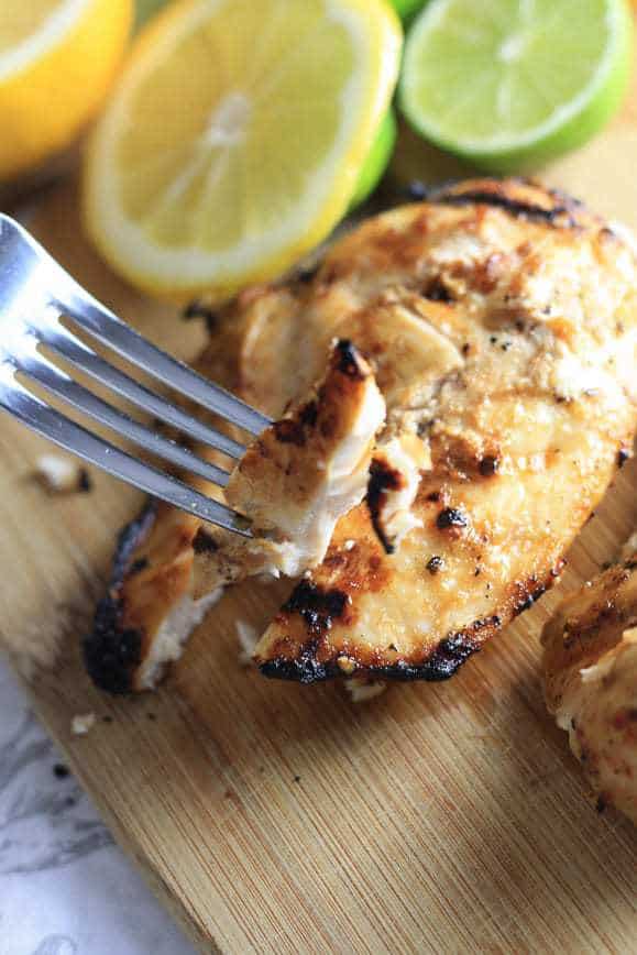 Lemon Grilled Chicken on a Cutiting Board being Sliced and Served with. Fork