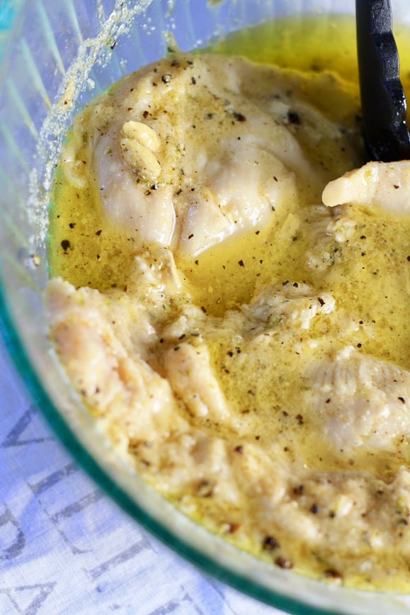 Bowl of Marinade (lemon, olive oil, lime juice, spices, etc) with chicken marinating in it. 