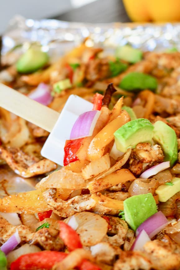 Chicken Sheet Pan Fajitas on a baking sheet topped with avocado, cilantro and red onion
