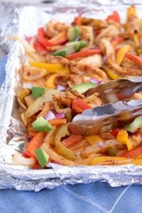 sheet pan fajitas tossed with tongs and garnished with avocado chunks