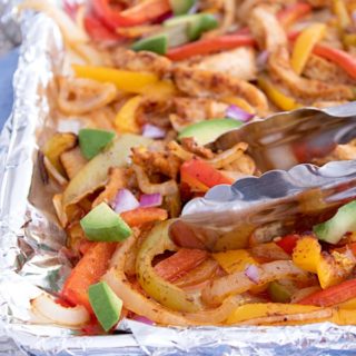 sheet pan fajitas tossed with tongs and garnished with avocado chunks