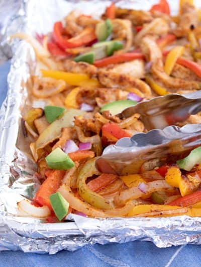 sheet pan fajitas tossed with tongs and garnished with avocado chunks