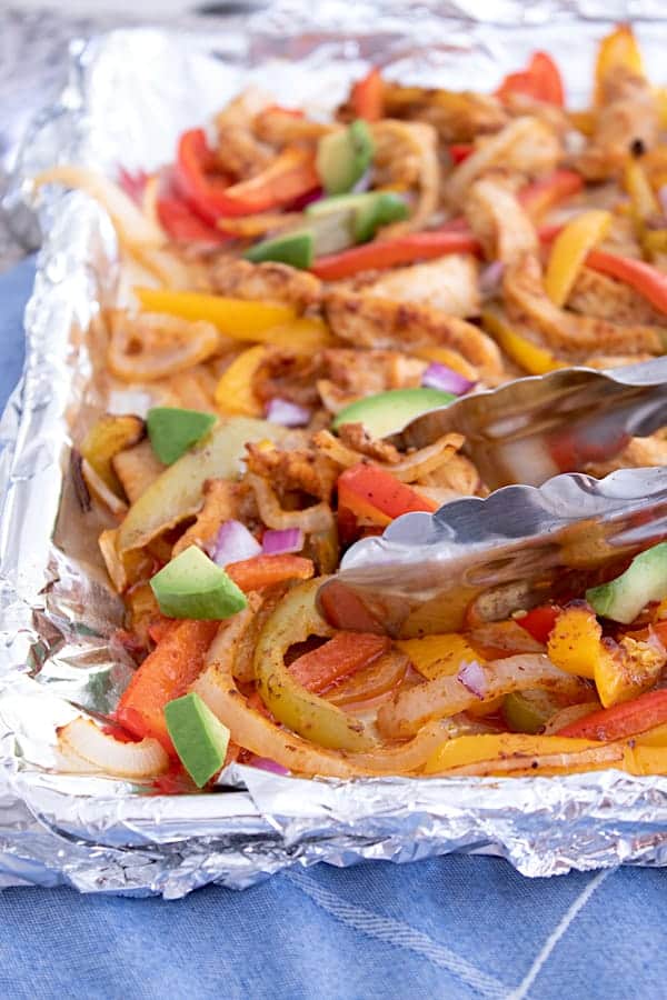 sheet pan fajitas tossed with tongs and garnished with avocado chunks