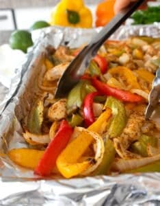 sheet pan fajitas being picked up with tongs