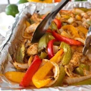 sheet pan fajitas being picked up with tongs