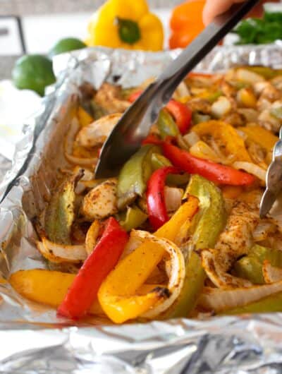 sheet pan fajitas being picked up with tongs