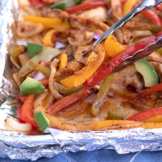 tongs grabbing fajitas on a sheet pan