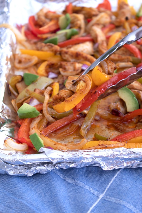 tongs grabbing fajitas on a sheet pan