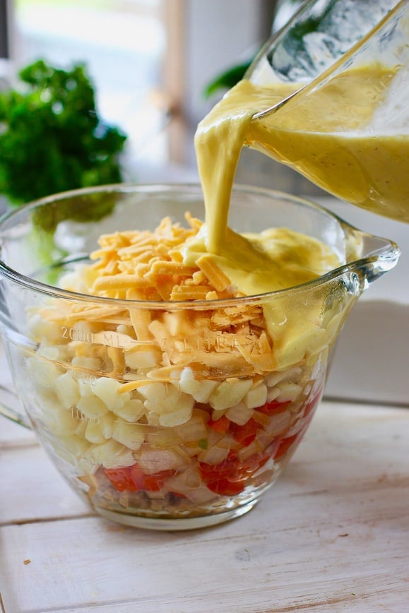 A bowl of sausage, hashbrowns and cheese being covered in beaten eggs