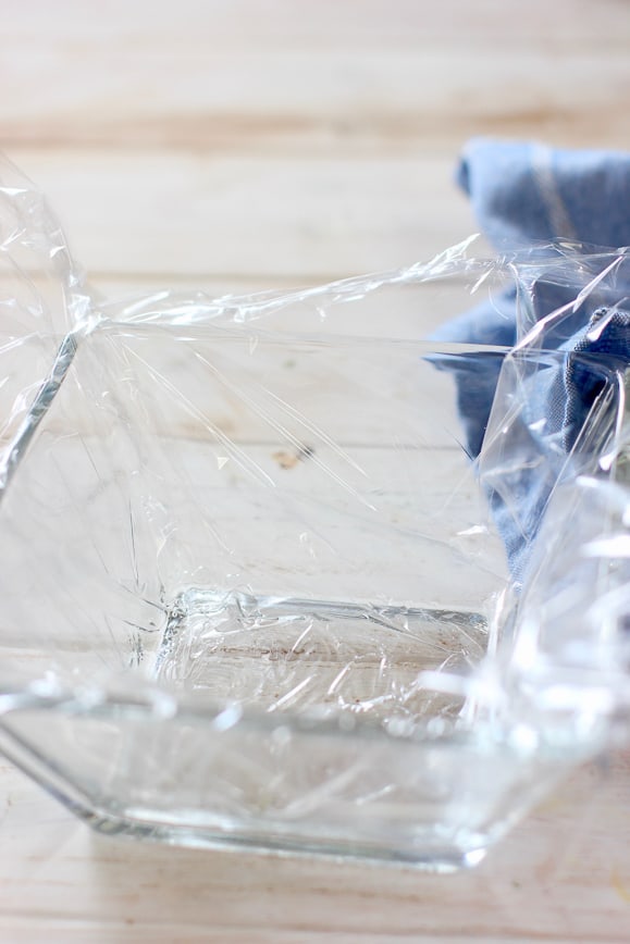 A clear square bowl with Saran Wrap in the inside of it.
