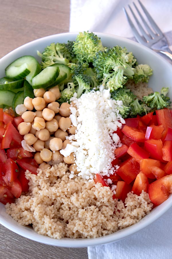 layered ingredients for couscous salad in a white porcelain bowl