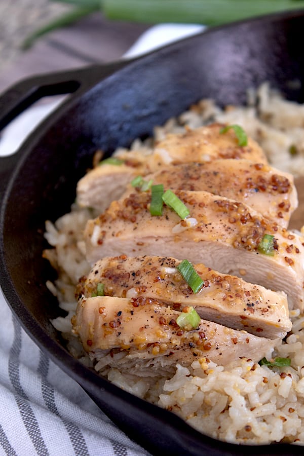 sliced honey mustard chicken breast with white rice in black cast iron pan