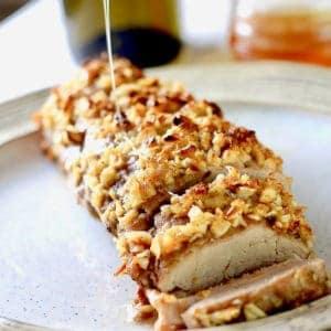 A pork loin on a tan ceramic plate crusted with garlic and brown sugar with honey drizzled over it