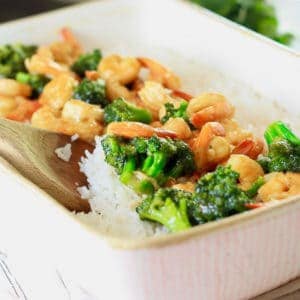 A light pink casserole dish filled with cooked white rice topped with shrimp and broccoli stir fry
