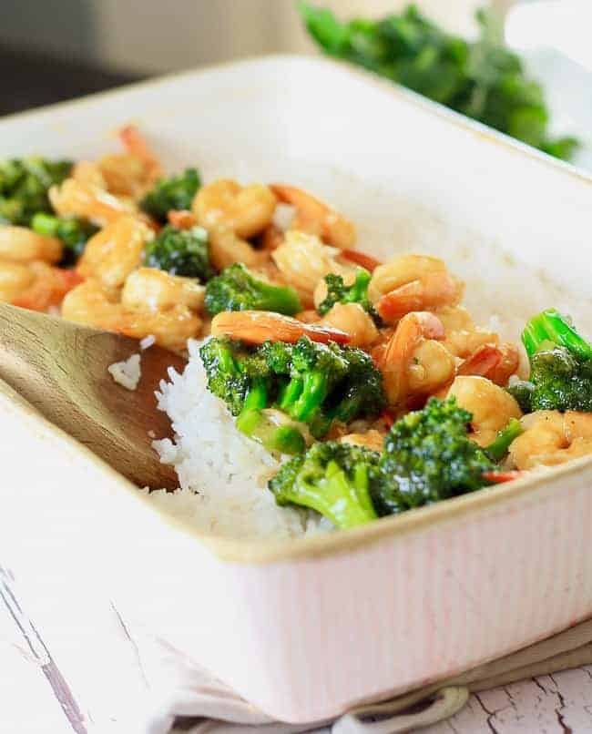 A light pink casserole dish filled with cooked white rice topped with shrimp and broccoli stir fry