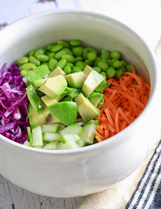 A white bowl filled with sliced veggies including avocado cucumber carrots and purple cabbage