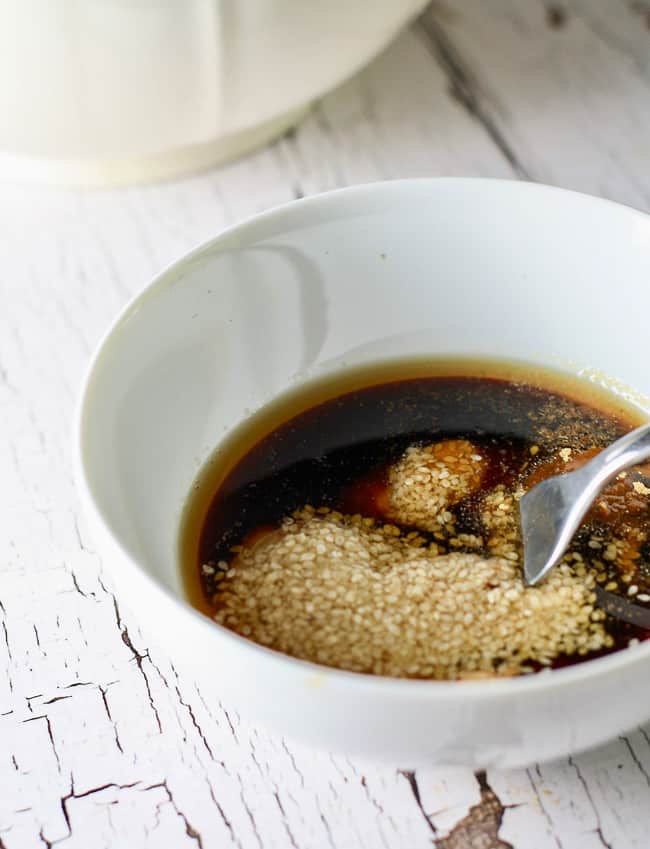 A white bowl filled with melted peanut butter, sesame oil, sesame seeds, and soy sauce