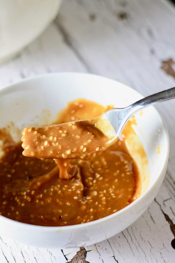 A white bowl with a silver fork showing a thick and creamy peanut sesame sauce