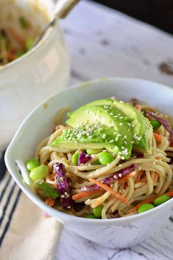 A white bowl filled with soba noodle salad and topped with avocado and sesame seeds