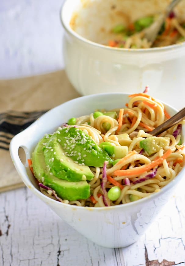 A white bowl filled with soba noodle salad toped with avocado and sesame seeds