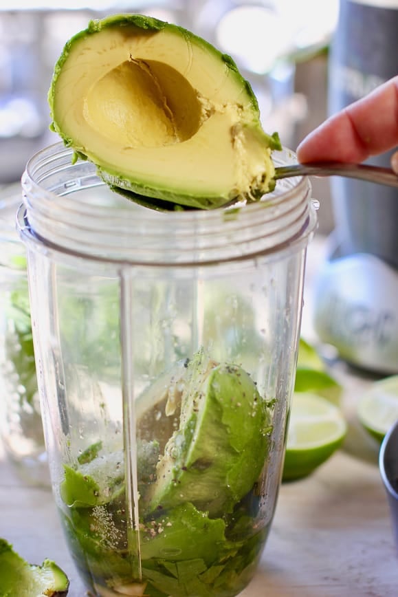 a blender jar with an avocado cilantro and olive oil getting ready to blend