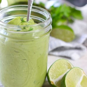 a mason jar full of emulsified avocado lime sauce with 2 lime wedges on the side