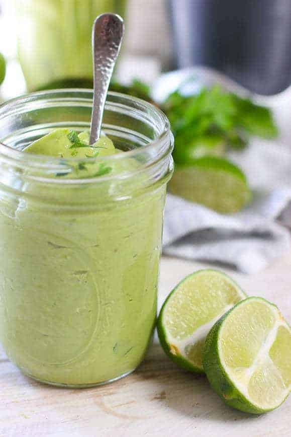 a mason jar full of emulsified avocado lime sauce with 2 lime wedges on the side