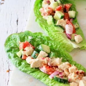A white wood washed board with romaine lettuce wraps filled with vegetables and chicken