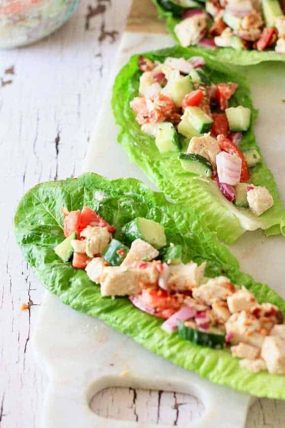 A white wood washed board with romaine lettuce wraps filled with vegetables and chicken
